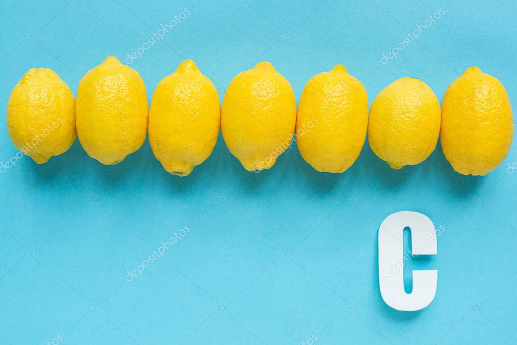 Top view of ripe yellow lemons and letter C on blue background