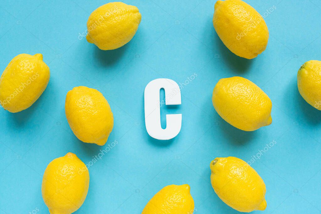 Top view of ripe yellow lemons and letter C on blue background