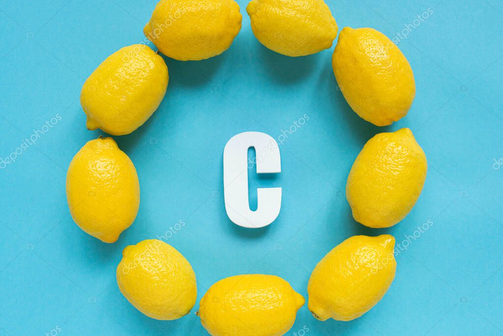 Top view of ripe yellow lemons around letter C on blue background