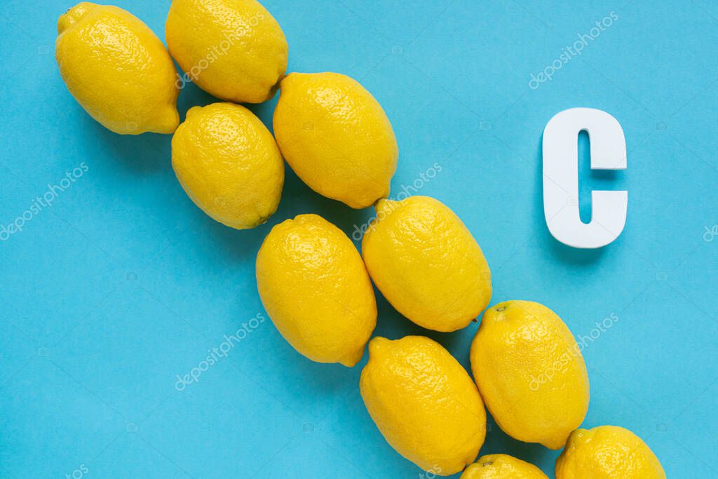Flat lay with ripe yellow lemons and letter C on blue background