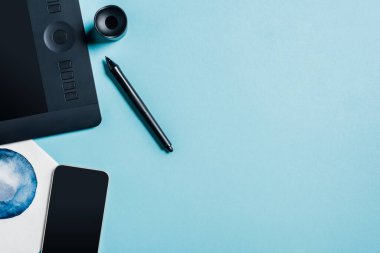 Grafik tabletinin üst görünümü, suluboya çizim ve mavi yüzeyde akıllı telefon