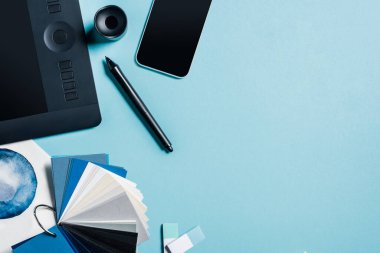 Grafik tableti, akıllı telefon, renk örnekleri ve mavi arkaplanda suluboya çizimlerinin üst görünümü