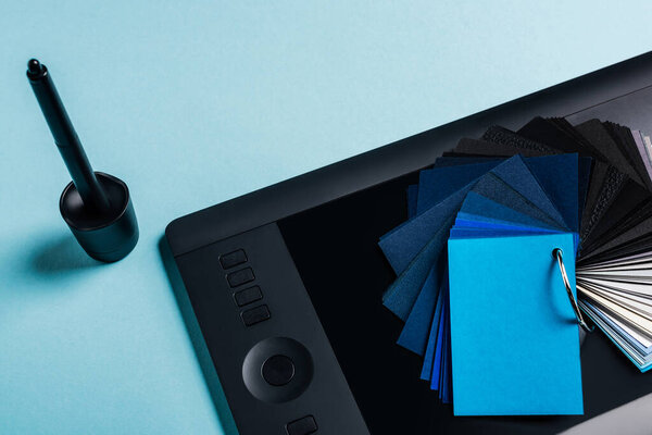 High angle view of color swatches, graphics tablet and stylus on blue background
