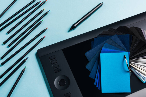 Top view of colorful swatches, graphics tablet and color pencils on blue background