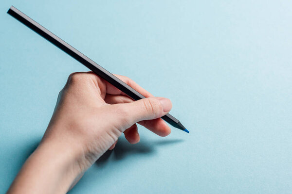 Cropped view of man holding pencil on blue background