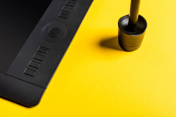 Close up view of stylus in stand and graphics tablet on yellow background