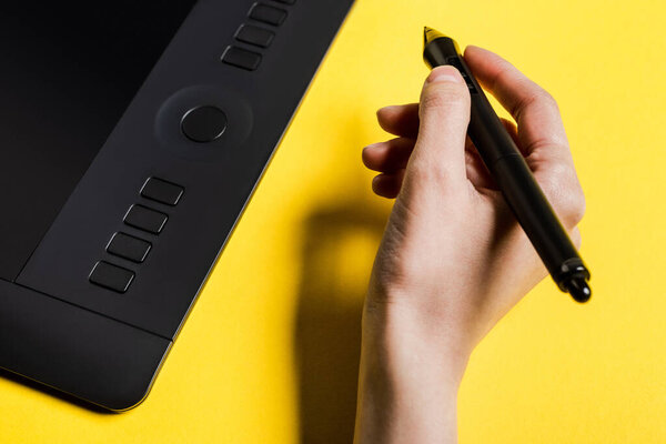 Cropped view of man holding stylus near graphics tablet on yellow surface