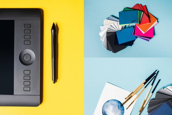 Коллаж графических планшетов, цветных образцов и кистей с акварелью на синей и желтой поверхности
