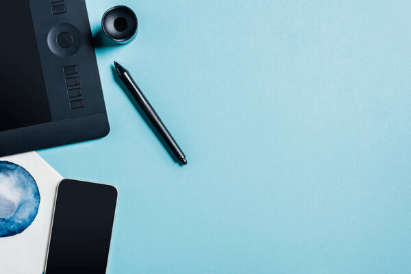 Top view of graphics tablet, watercolor drawing and smartphone on blue surface