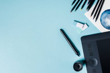 Stylus, renk kalemleri ve mavi arkaplan üzerine suluboya çizimi olan grafik tabletinin üst görünümü