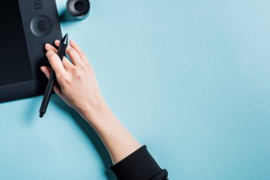 Stylus 'u tutan tasarımcının üst görünümü ve mavi arkaplan üzerinde grafik tableti kullanılması