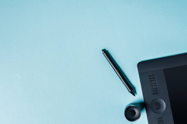 Top view of graphics tablet with stylus on blue background