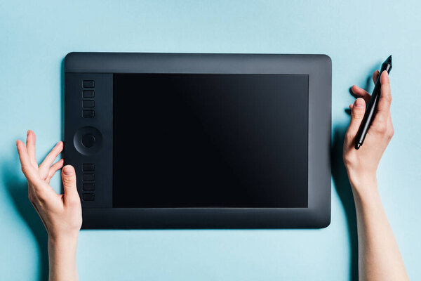 Cropped view of man holding stylus near graphics tablet on blue background