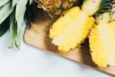 Beyaz arka planda tahta kesme tahtasındaki sulu ananas yarımlarının üst görüntüsü