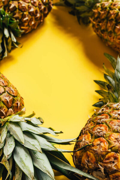 selective focus of fresh ripe pineapples with green leaves on yellow background