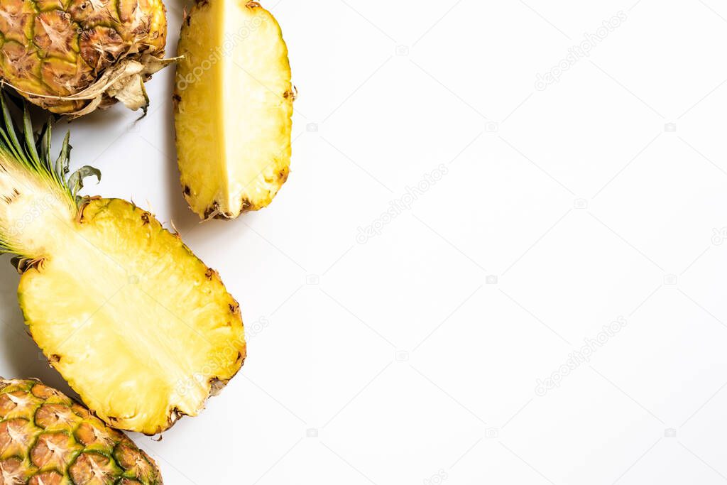 top view of cut and whole ripe pineapples with green leaves on white background