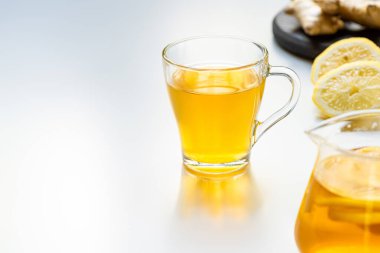 Beyaz arka planda limon dilimleri olan cam bardaktaki sıcak çayın seçici odağı