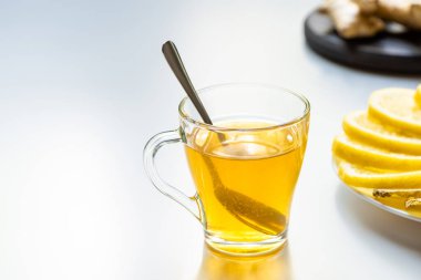 Beyaz arka planda limon dilimlerinin yanında kaşıkla cam bardaktaki sıcak çayın seçici odağı