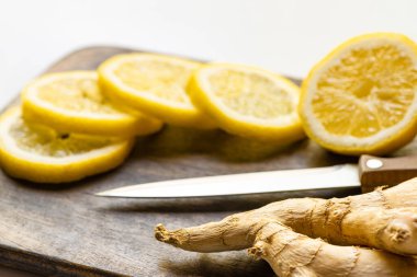 Sıcak zencefil kökü seçici odak noktası, ahşap kesme tahtasındaki limon beyaz arka planda bıçakla