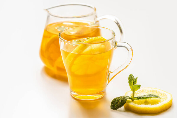 селективный фокус горячего чая в стакане и чайник возле лимона и мяты на белом фоне

