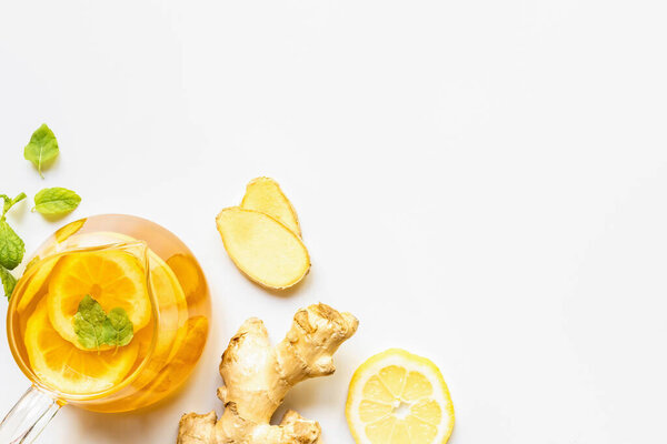 сверху вид на горячий чай около корня имбиря, лимона и мяты на белом фоне
