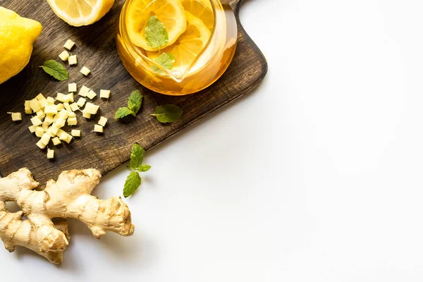 Zencefil kökü yakınlarındaki sıcak çay, limon ve nane, beyaz arka planda tahta kesme tahtası.