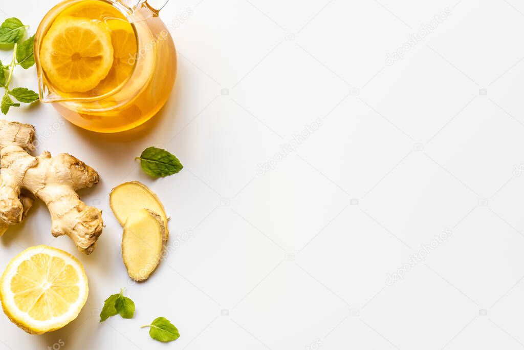 top view of hot tea in glass teapot near ginger root, lemon and mint on white background