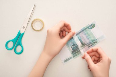 KYIV, UKRAINE - MARCH 25, 2020: cropped view of woman repairing ruble banknote with duct tape near scissors isolated on white clipart