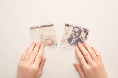 KYIV, UKRAINE - 25 Mart 2020: Yırtık Japon yen banknotuna dokunan kadının üst görünümü beyaz üzerine izole edilmiş