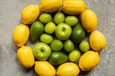 Gri beton yüzeyde daire içine alınmış renkli elma, avokado, limon ve limonların üst görünümü