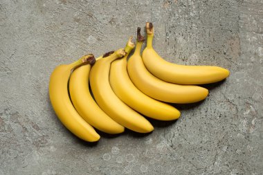 top view of colorful delicious bananas on grey concrete surface clipart