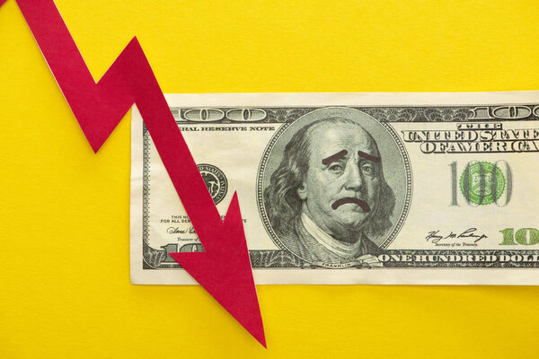 KYIV, UKRAINE - MARCH 25, 2020: top view of dollar banknote with sad face drawing near red crisis graph isolated on yellow 