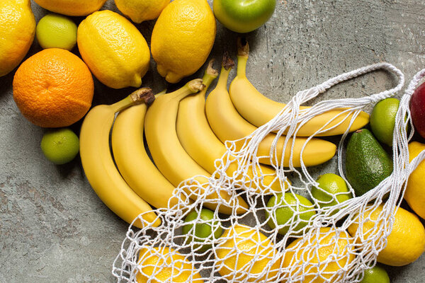top view of colorful delicious fruits and string bag on grey concrete surface