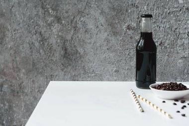 Şişe içinde buzlu soğuk demlenmiş kahvenin seçici odağı pipet ve beyaz masada kahve çekirdekleri içmek.
