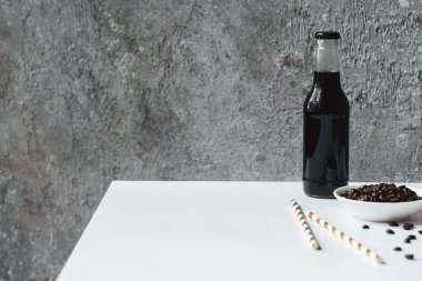 selective focus of cold brew coffee with ice in bottle near drinking straws and coffee beans on white table clipart