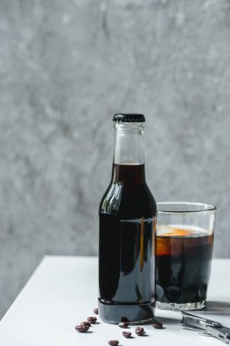 Bardakta buzlu soğuk kahve ve kahve çekirdeğinin yanında şişe ve beyaz masada da açacağı.