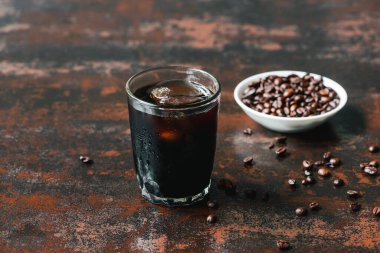 Paslı yüzeydeki kahve çekirdeklerinin yanında buzlu soğuk demlenmiş kahvenin seçici odağı.