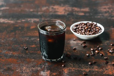 selective focus of cold brew coffee with ice in glass near coffee beans on rusty surface clipart