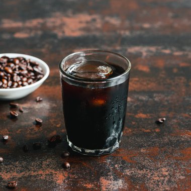 selective focus of cold brew coffee with ice in glass near coffee beans on rusty surface clipart