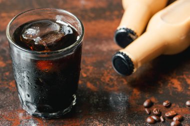Bardakta buzlu soğuk kahve ve paslı yüzeyde kahve çekirdeğinin yanında şişe olan seçici bir odak noktası.