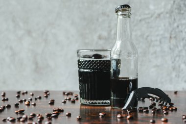 Şişede soğuk kahve, açacağa yakın bardak ve kahve çekirdeği.