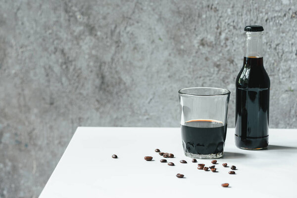 cold brew coffee in glass and bottle near coffee beans on white table