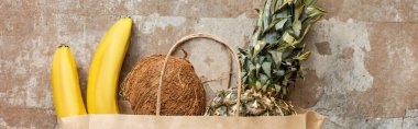top view of tropical fresh fruits in paper bag on weathered surface, panoramic crop clipart
