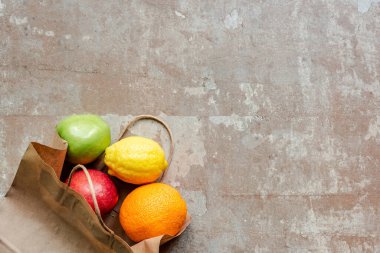 Kırmızı ve yeşil elmalı kağıt torbanın üst görüntüsü, limon ve turuncu yıpranmış bej yüzey