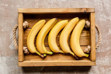 top view of ripe bananas in wooden box on weathered surface clipart