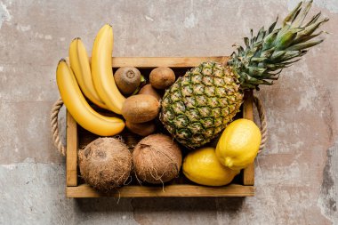 top view of ripe tropical fruits in wooden box on weathered surface clipart