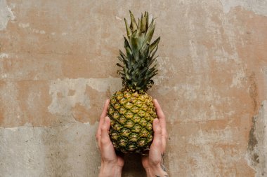 Yıpranmış yüzeyde olgun ananas tutan kadın manzarası.