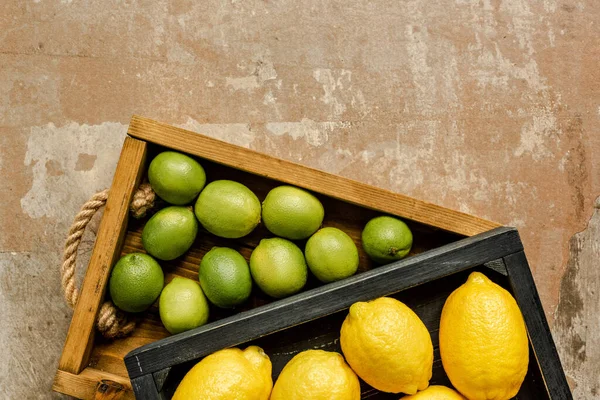 top view of lemons and limes in wooden boxes on weathered surface