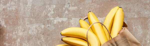 вид сверху на бумажный пакет с бананами на бежевой выветриваемой поверхности, панорамный урожай
