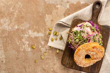 Etli taze simit, kırmızı soğan ve ahşap filizler peçetede kesme tahtası ve bej rengi yüzey üzerinde balkabağı tohumları.